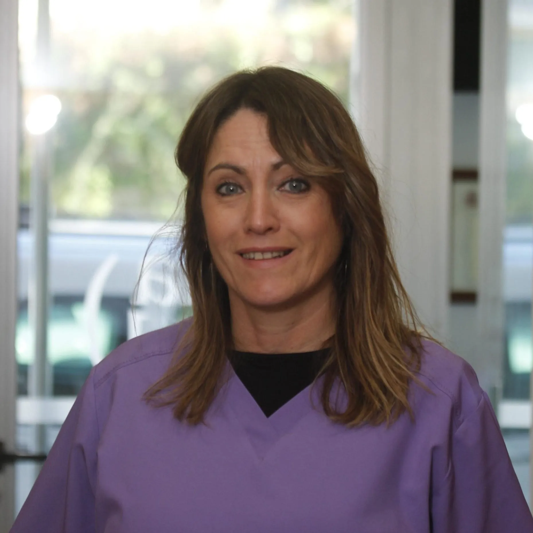 Profesional de recepción de Enamel Clínica Dental sonriendo con uniforme lila
