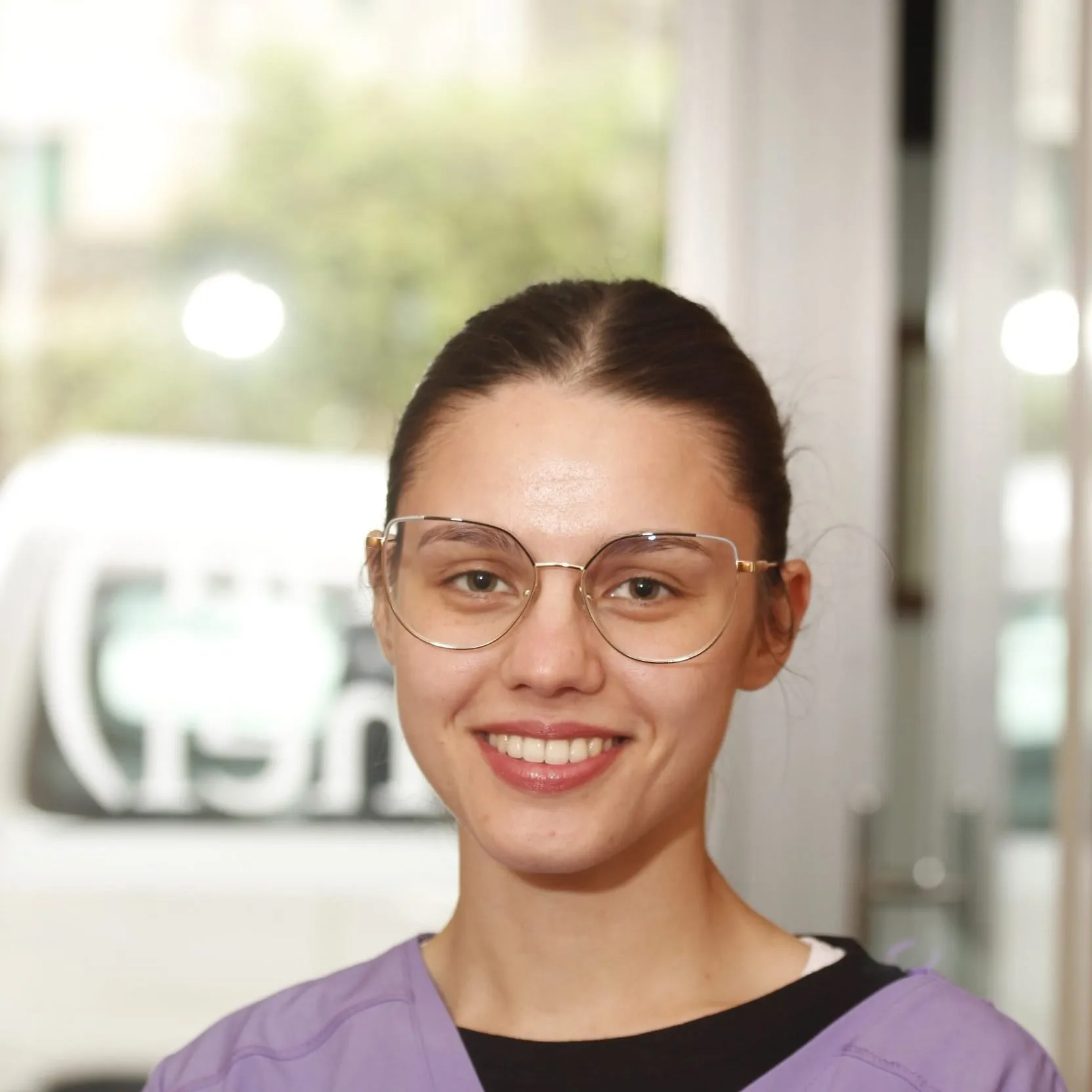 Auxiliar clínica de Enamel Clínica Dental con uniforme lila y la chapa de la clínica