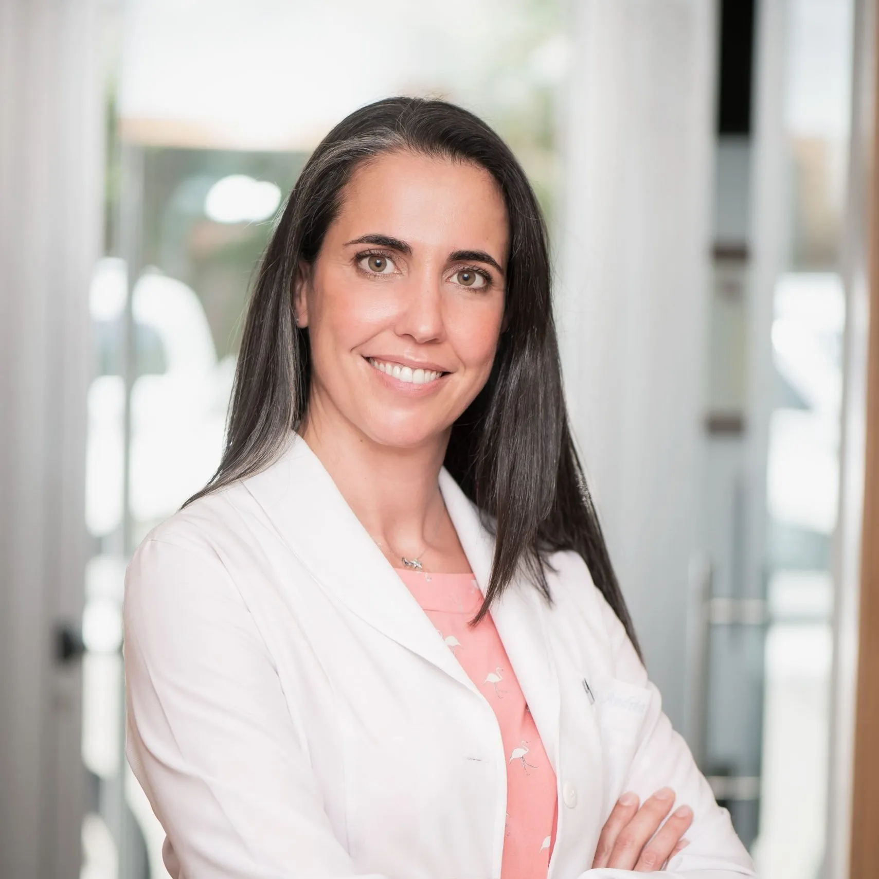 Odontóloga de Enamel Clínica Dental con bata blanca y los brazos cruzados en la entrada